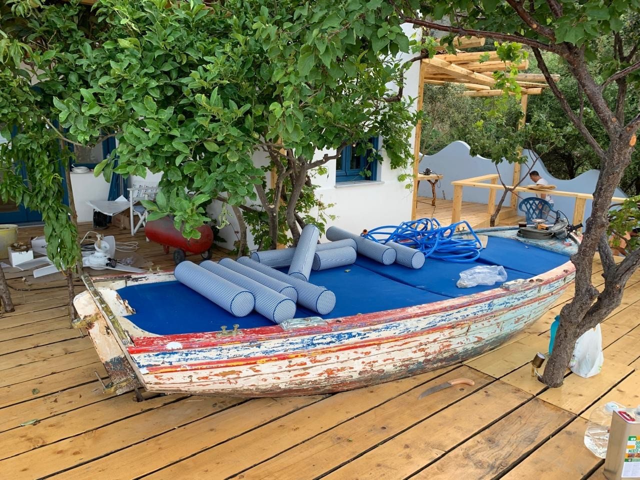 Fishing-boat daybed with blue cushions framed by trees and the sea